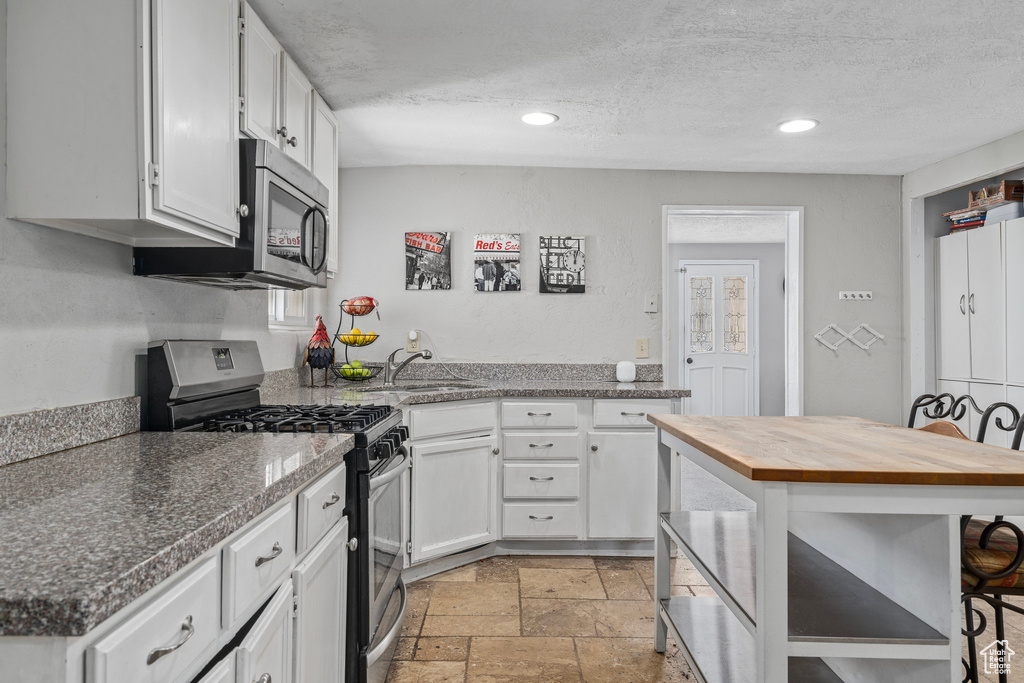 Kitchen featuring stainless steel appliances, white cabinetry, sink, light tile patterned floors, and a breakfast bar