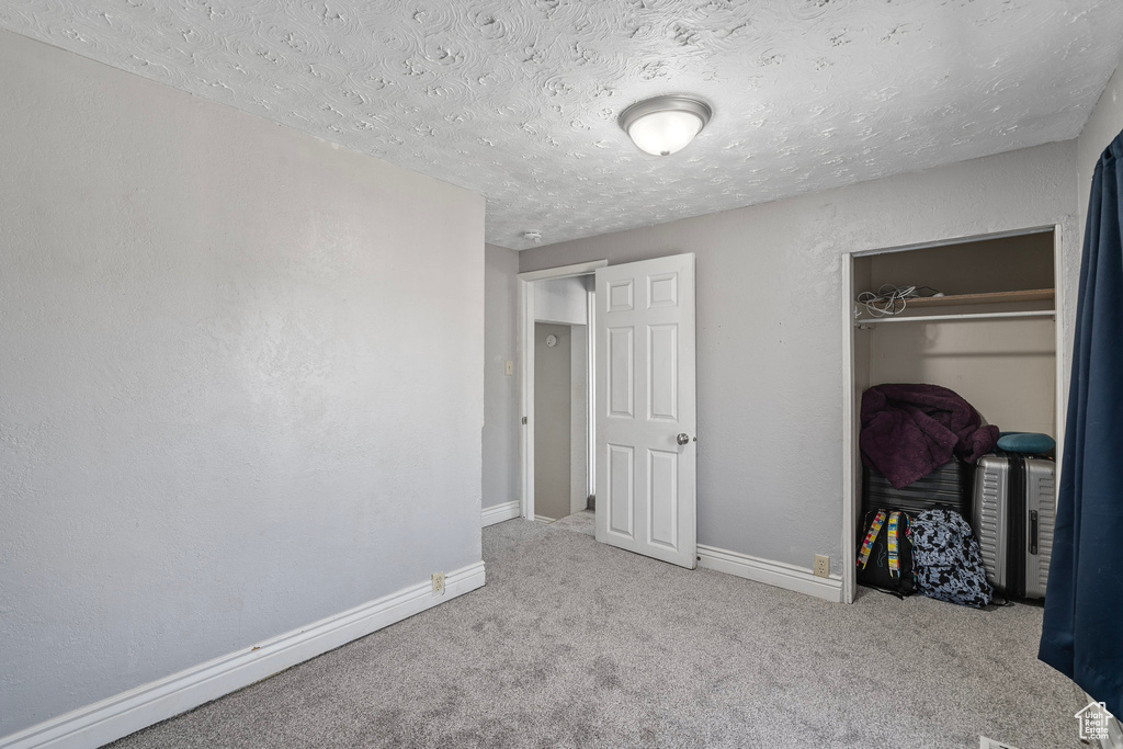 Unfurnished bedroom with light colored carpet, a closet, and a textured ceiling