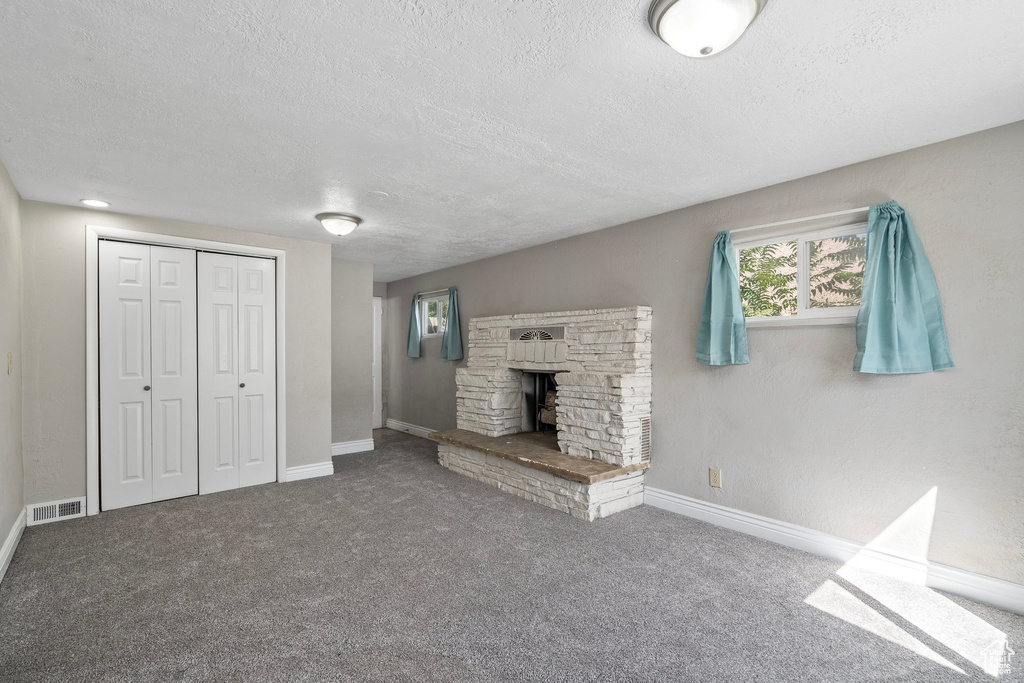 Unfurnished living room with carpet flooring, a textured ceiling, and a fireplace