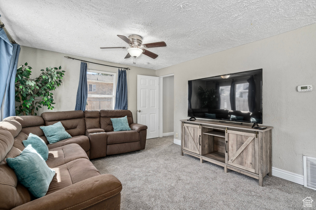 Carpeted living room with ceiling fan and a textured ceiling