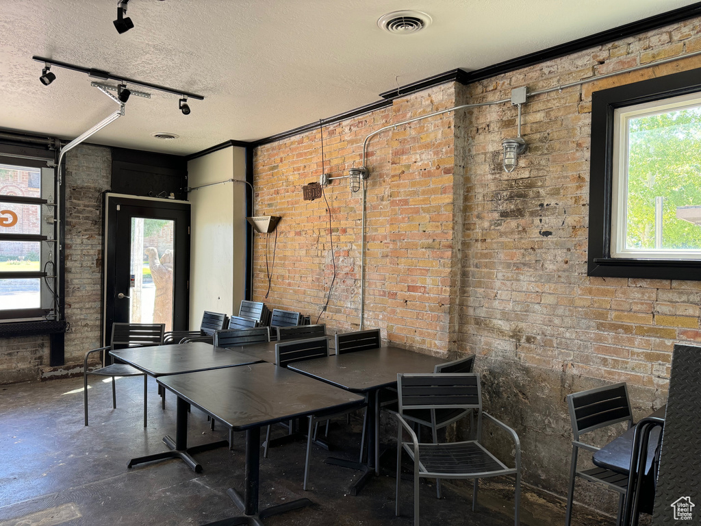 Dining space featuring track lighting, a textured ceiling, and brick wall