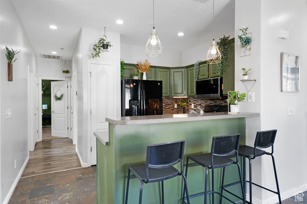 Kitchen with green cabinets, black fridge with ice dispenser, backsplash, a kitchen bar, and dark hardwood / wood-style floors