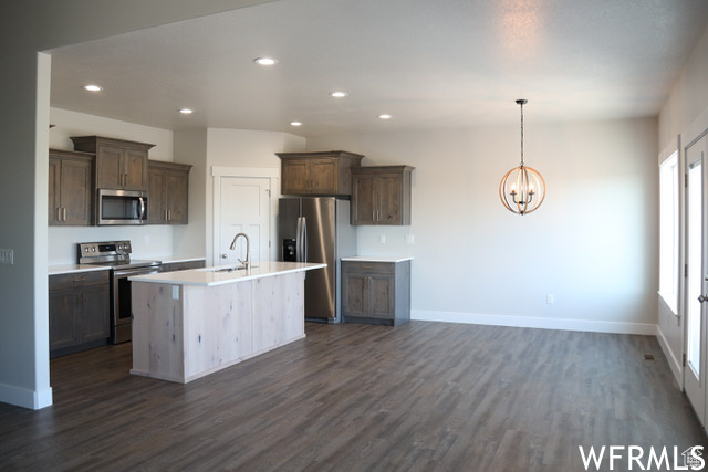 Kitchen featuring dark hardwood / wood-style flooring, an island with sink, stainless steel appliances, sink, and a chandelier