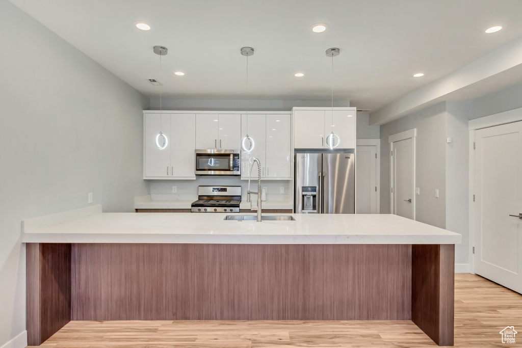 Kitchen with decorative light fixtures, stainless steel appliances, sink, light wood-type flooring, and white cabinets