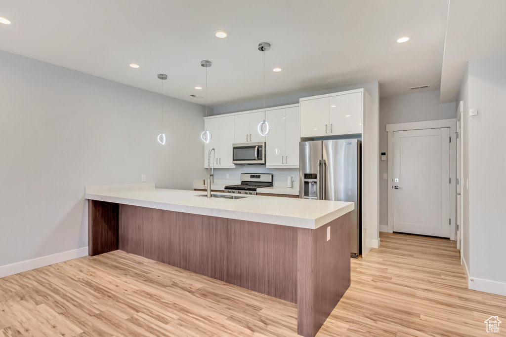 Kitchen with decorative light fixtures, kitchen peninsula, appliances with stainless steel finishes, white cabinets, and light hardwood / wood-style floors