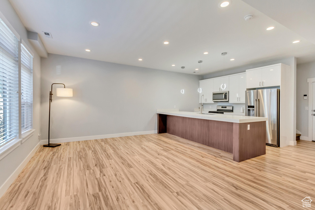 Kitchen with light wood-type flooring, appliances with stainless steel finishes, and white cabinets