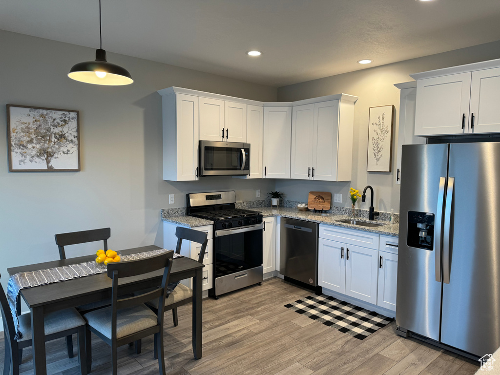 Kitchen featuring decorative light fixtures, appliances with stainless steel finishes, light hardwood / wood-style floors, sink, and white cabinets