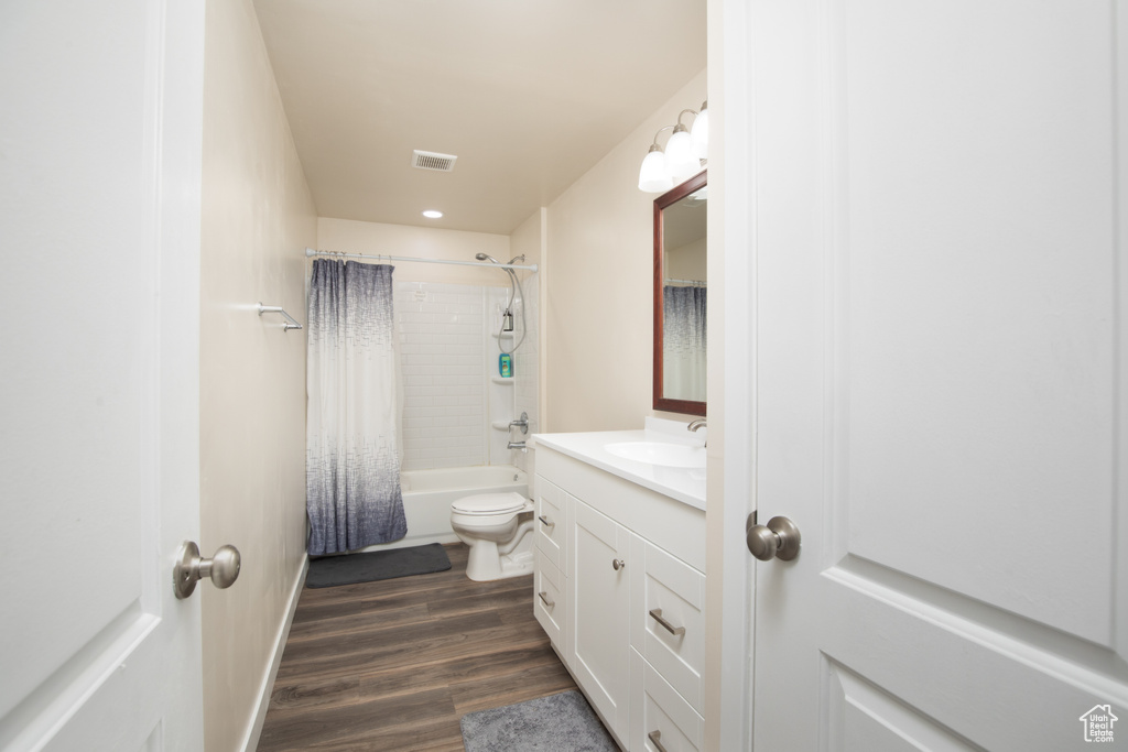 Full bathroom featuring hardwood / wood-style floors, toilet, shower / tub combo with curtain, and vanity