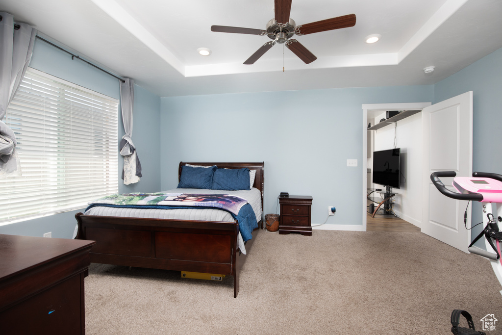 Carpeted bedroom featuring a tray ceiling and ceiling fan