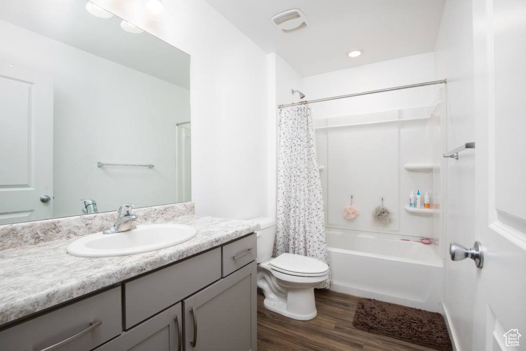 Full bathroom with hardwood / wood-style floors, toilet, shower / bathtub combination with curtain, and vanity