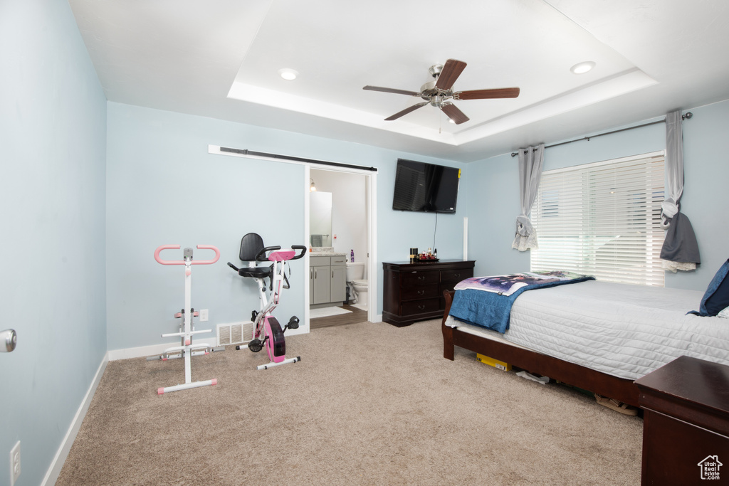 Carpeted bedroom with a raised ceiling, ceiling fan, and ensuite bath