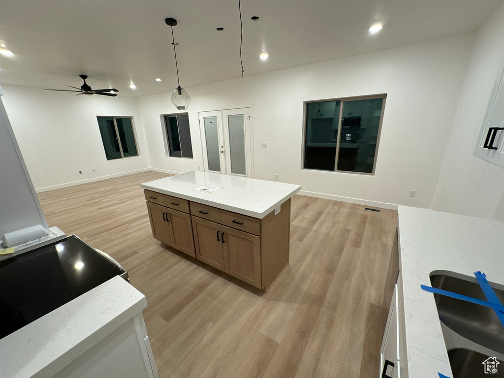 Kitchen with ceiling fan, light stone counters, decorative light fixtures, a center island, and light hardwood / wood-style floors