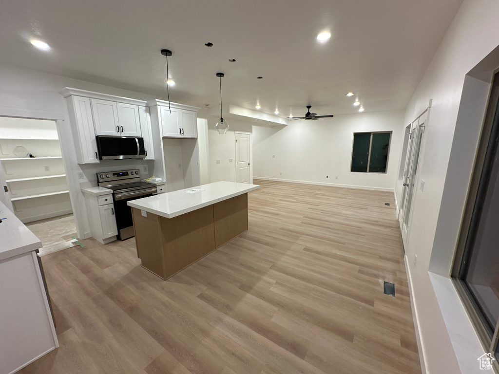 Kitchen with appliances with stainless steel finishes, white cabinetry, a center island, and ceiling fan