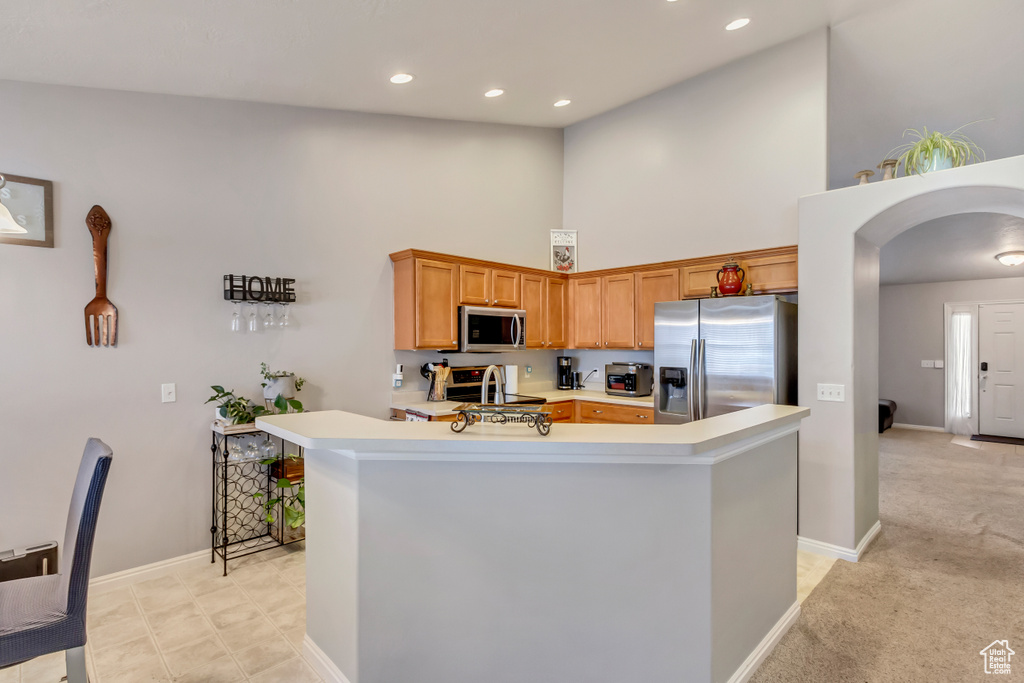 Kitchen featuring light carpet, kitchen peninsula, a high ceiling, and stainless steel appliances