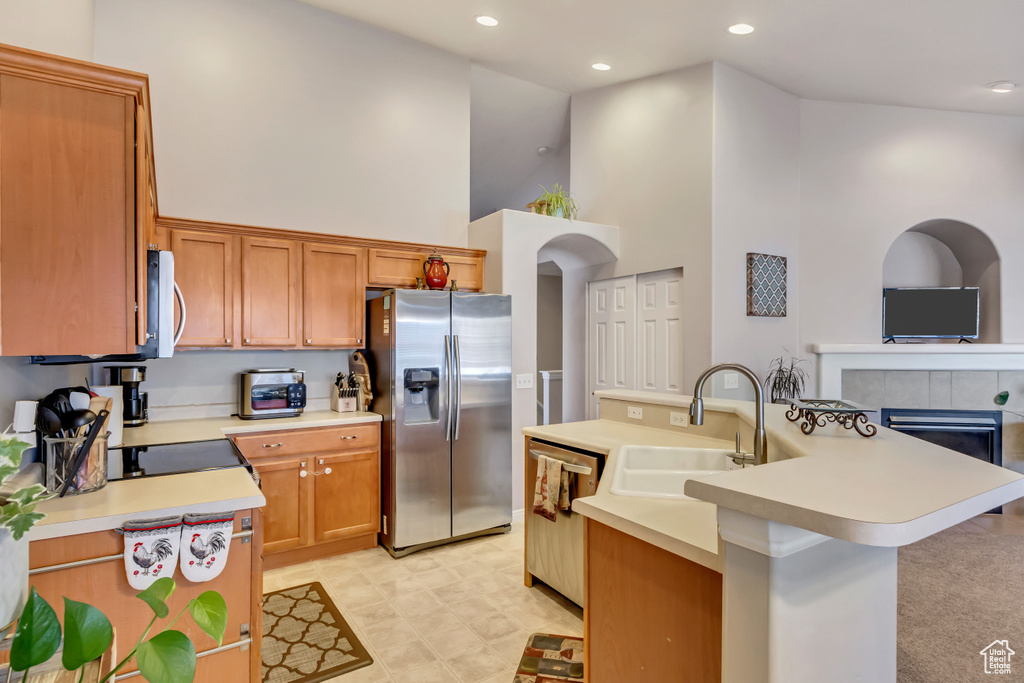 Kitchen with light tile patterned flooring, high vaulted ceiling, sink, a kitchen island with sink, and stainless steel appliances