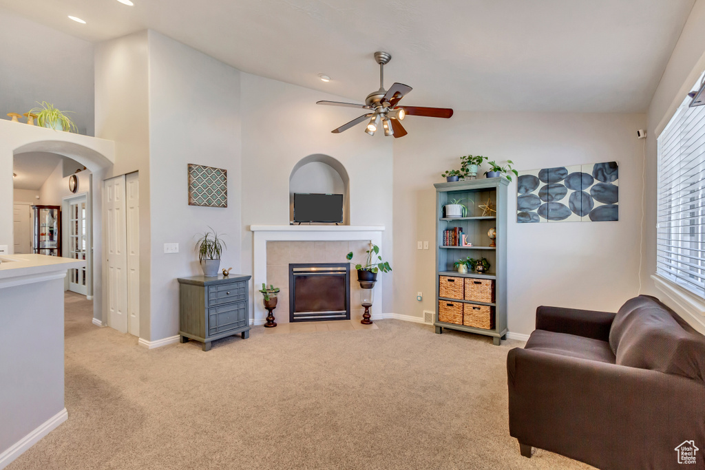 Living room with ceiling fan, a tiled fireplace, light carpet, and lofted ceiling