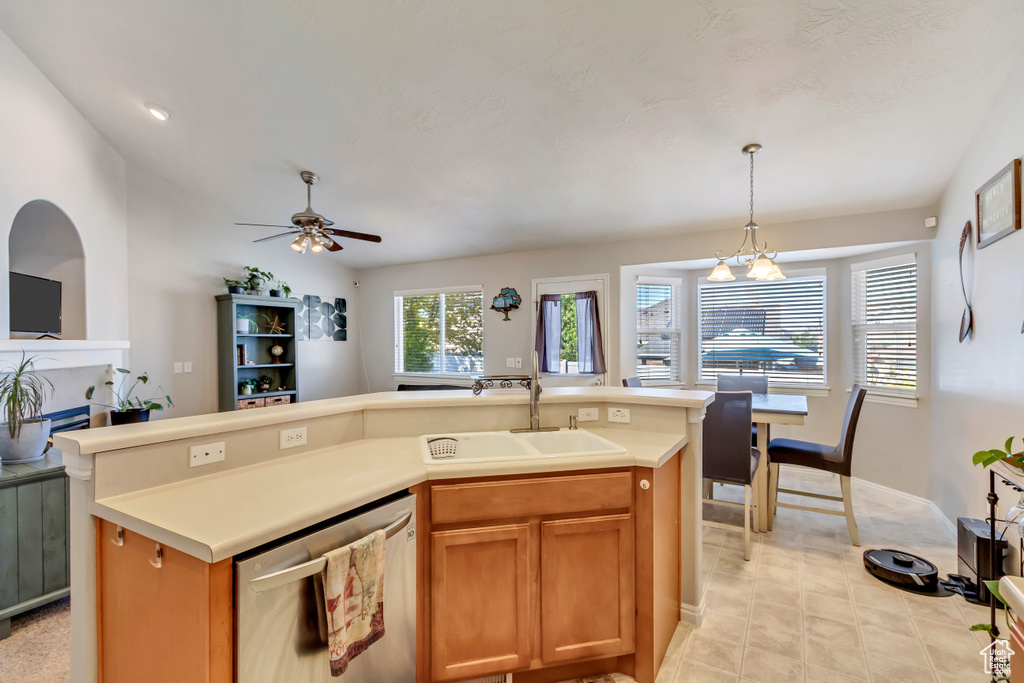 Kitchen with light tile patterned flooring, sink, ceiling fan with notable chandelier, stainless steel dishwasher, and a center island with sink