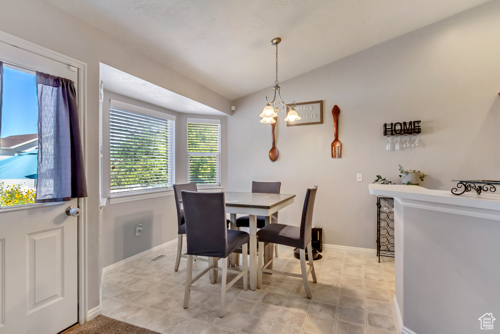 Dining area featuring light tile patterned flooring, vaulted ceiling, and a chandelier