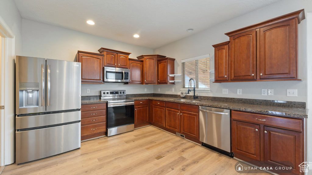 Kitchen featuring appliances with stainless steel finishes, light hardwood / wood-style flooring, sink, and dark stone counters