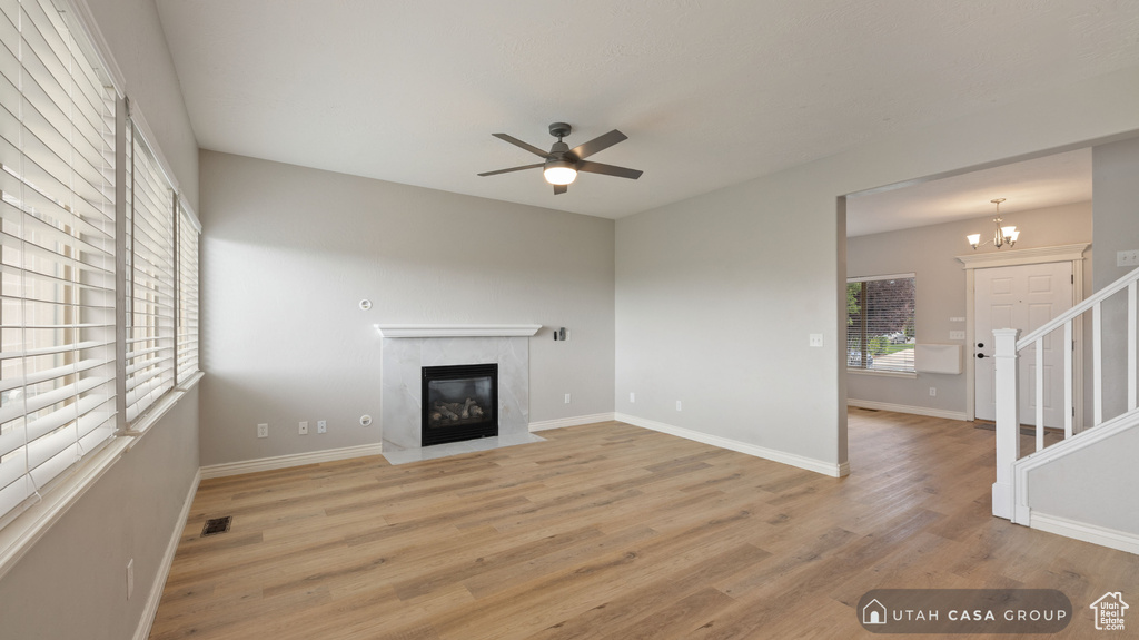 Unfurnished living room featuring ceiling fan with notable chandelier, a high end fireplace, and light wood-type flooring