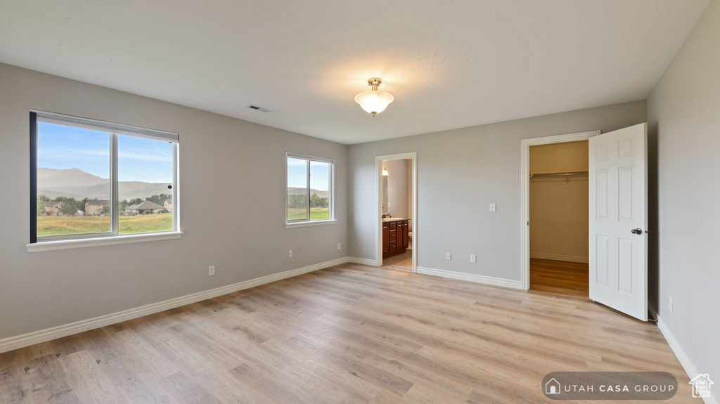 Unfurnished bedroom featuring a mountain view, light hardwood / wood-style floors, ensuite bath, a spacious closet, and a closet