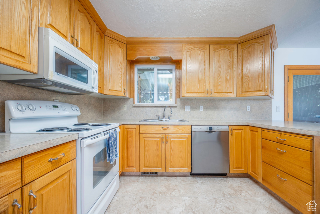 Kitchen featuring backsplash, sink, light tile patterned floors, and white appliances