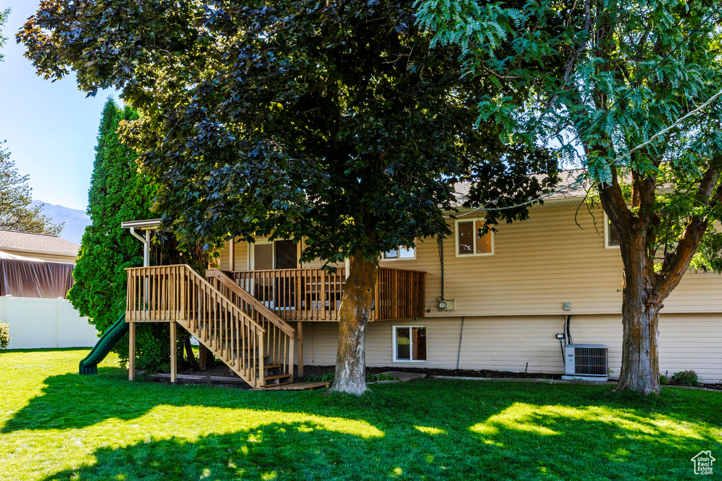 Rear view of house featuring cooling unit, a lawn, and a deck