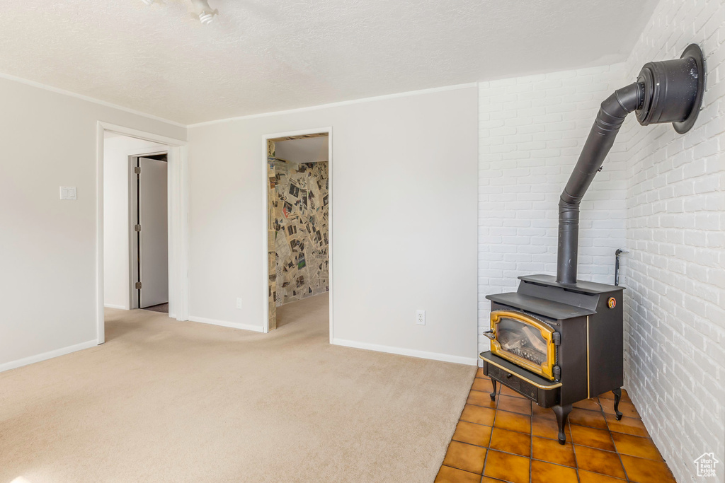 Living room with a textured ceiling, brick wall, a wood stove, and tile patterned flooring