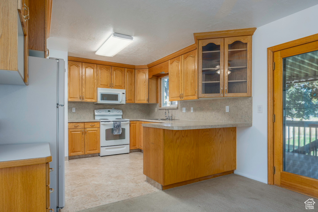 Kitchen featuring white appliances, light tile patterned floors, tasteful backsplash, kitchen peninsula, and sink