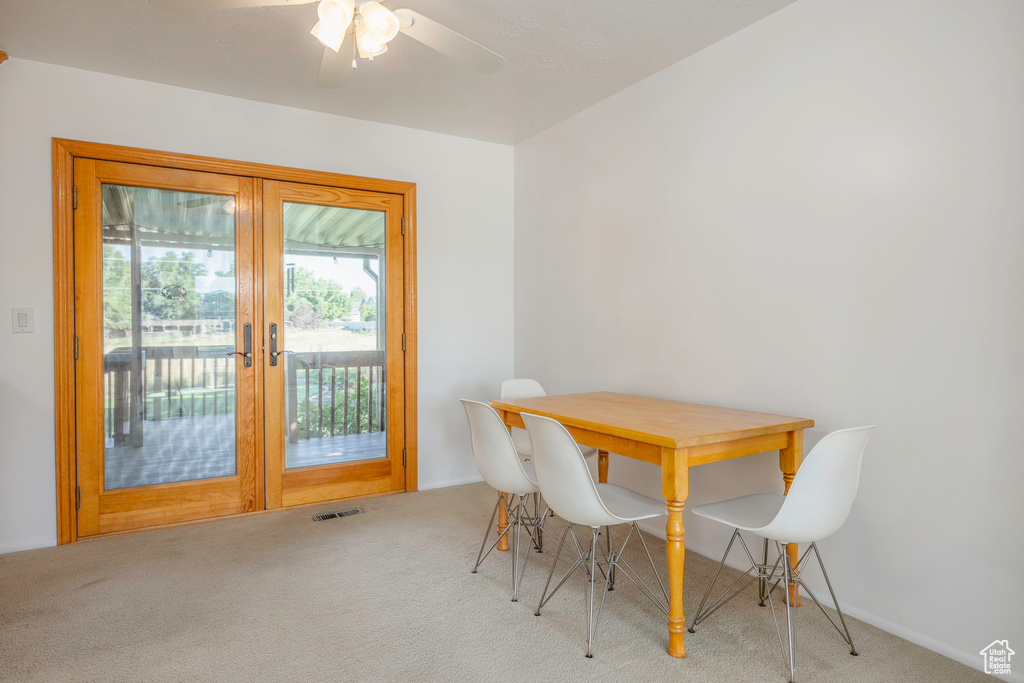 Carpeted dining area featuring ceiling fan and french doors