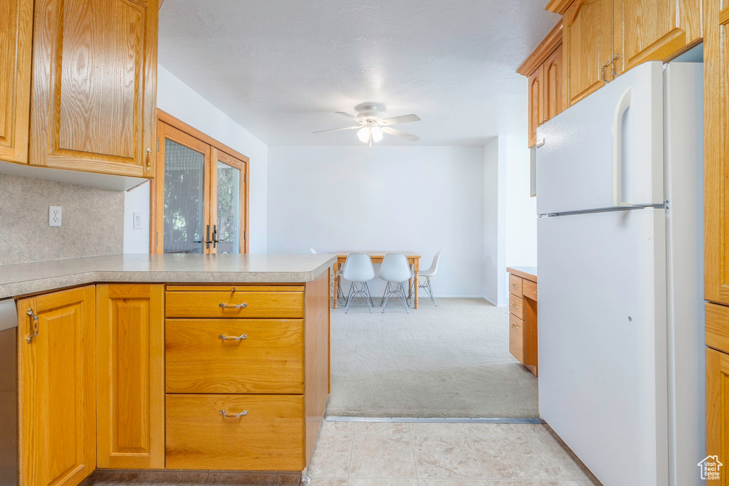 Kitchen featuring white refrigerator, kitchen peninsula, ceiling fan, and light tile patterned flooring