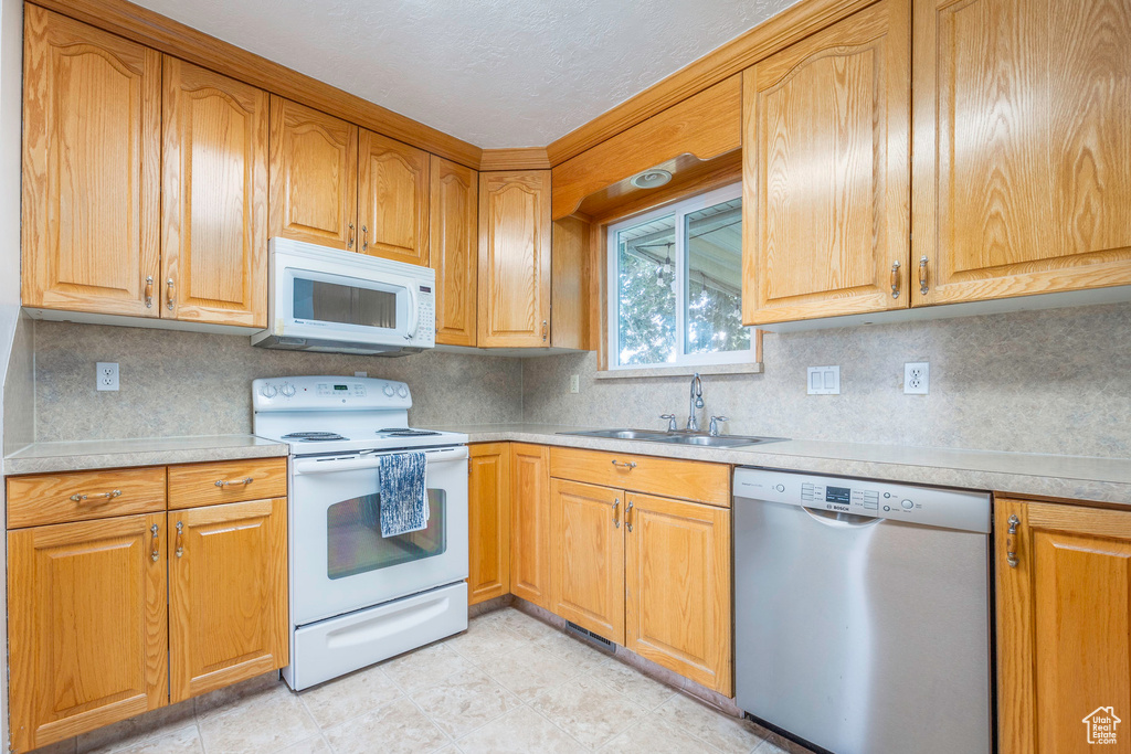 Kitchen with white appliances, sink, light tile patterned flooring, and tasteful backsplash