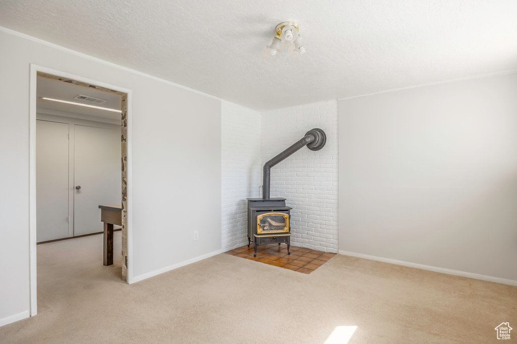 Unfurnished bedroom featuring a wood stove, a textured ceiling, light carpet, and brick wall