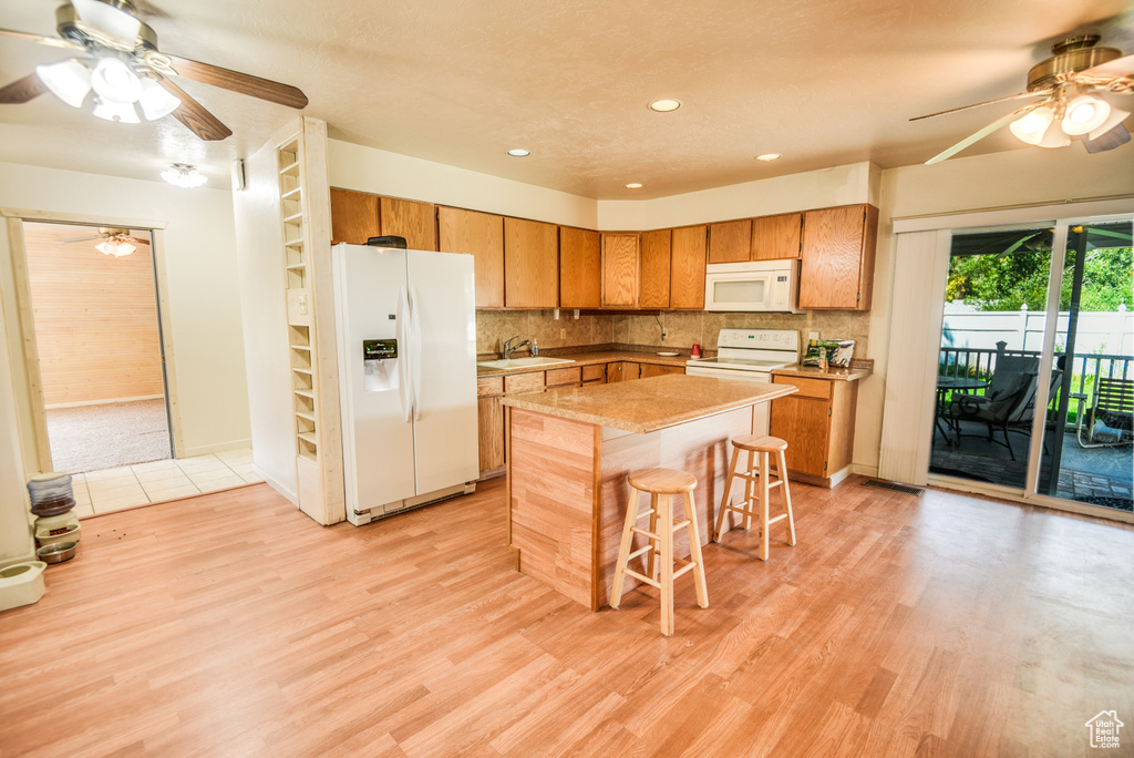 Kitchen featuring a center island, ceiling fan, light wood-type flooring, and white appliances