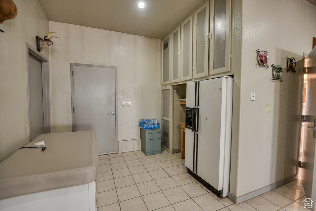 Kitchen featuring light tile patterned floors, white refrigerator with ice dispenser, and white cabinetry