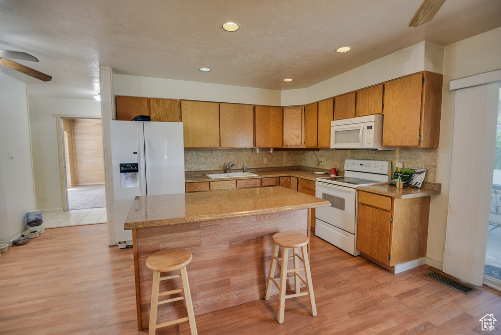 Kitchen featuring white appliances, a kitchen bar, sink, ceiling fan, and light hardwood / wood-style floors