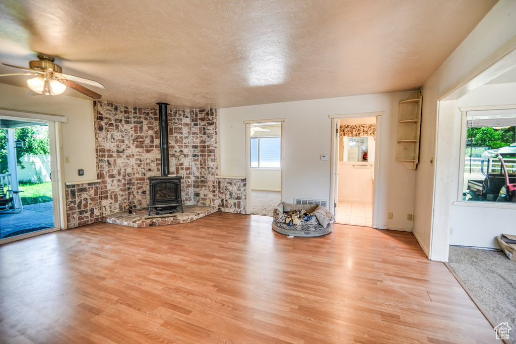 Unfurnished living room featuring brick wall, ceiling fan, a wood stove, and light hardwood / wood-style floors