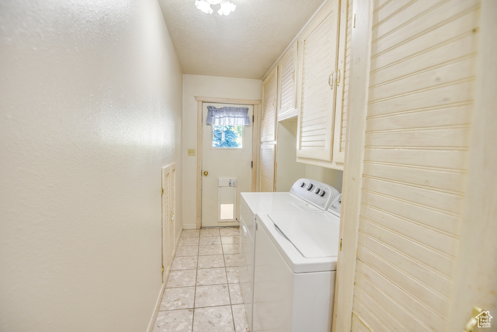 Laundry room with a textured ceiling, cabinets, independent washer and dryer, and light tile patterned flooring