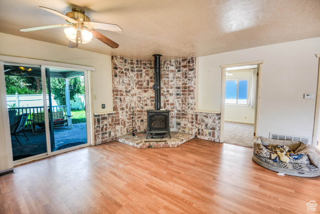Unfurnished living room featuring hardwood / wood-style floors, a textured ceiling, a wood stove, ceiling fan, and brick wall