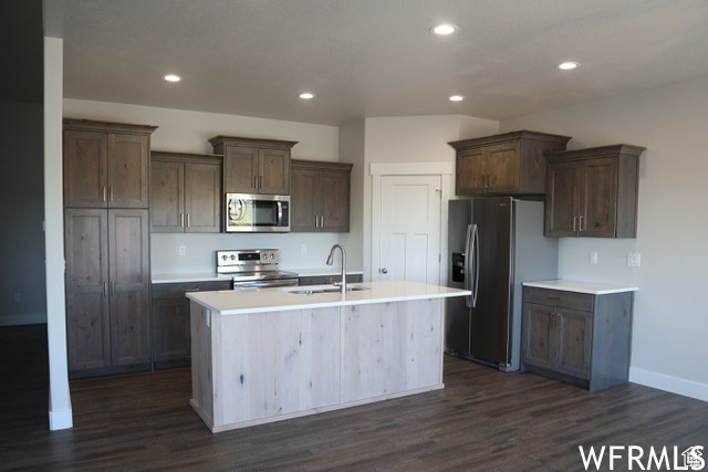 Kitchen featuring an island with sink, dark wood-type flooring, sink, and appliances with stainless steel finishes