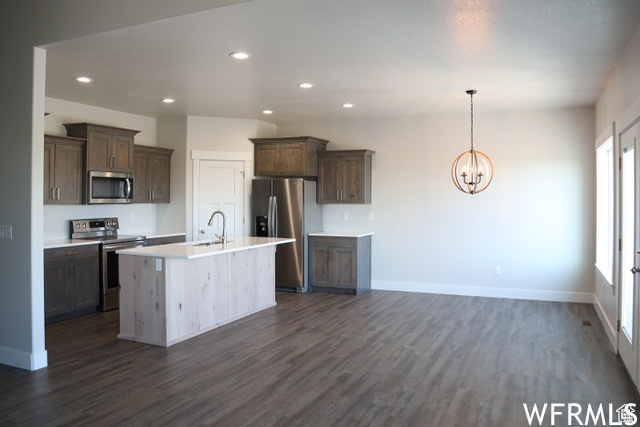 Kitchen with stainless steel appliances, a notable chandelier, sink, an island with sink, and dark wood-type flooring