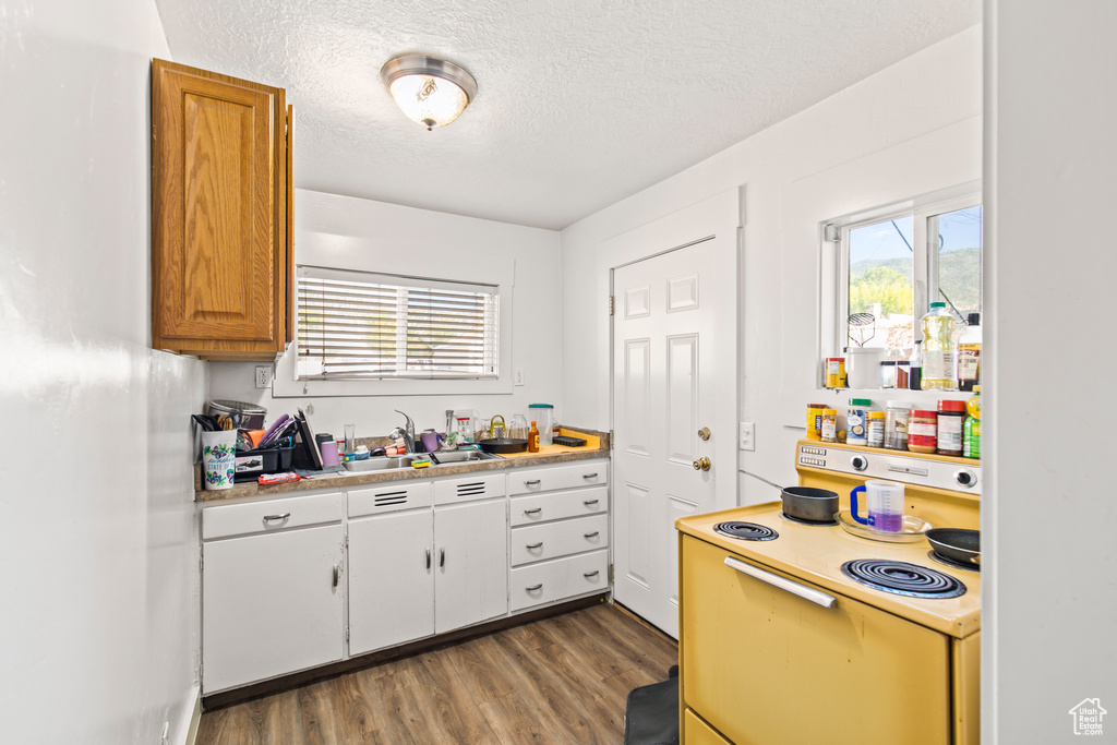 Kitchen with a textured ceiling, white range with electric stovetop, sink, and light hardwood / wood-style floors