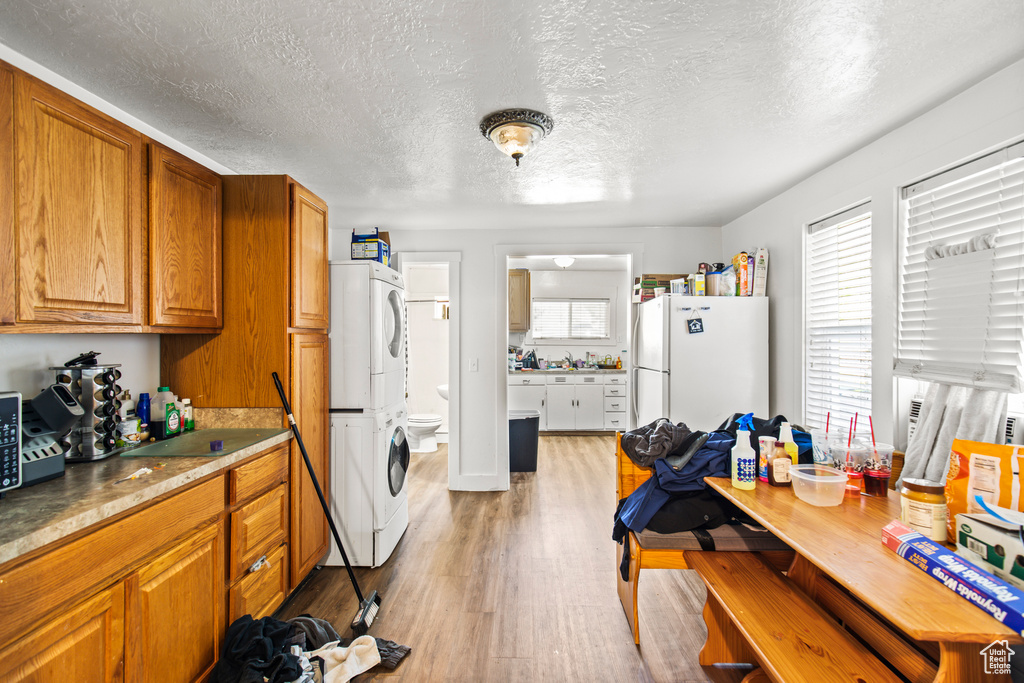 Kitchen with a textured ceiling, white fridge, stacked washer / dryer, and light hardwood / wood-style floors