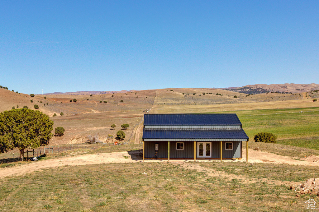 Rear view of house with a rural view, an outdoor structure, and a mountain view