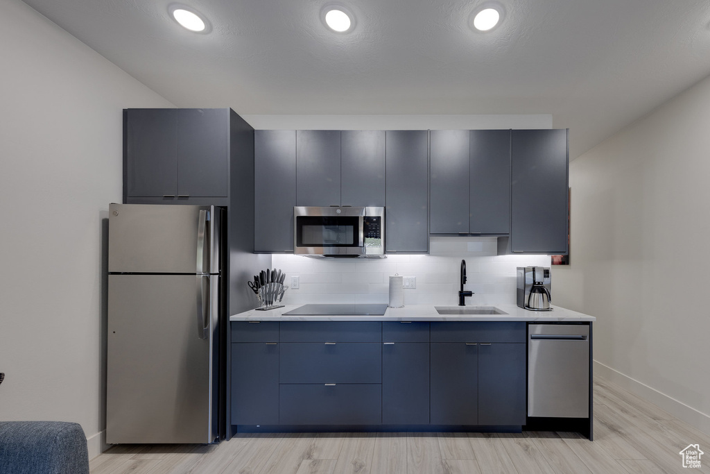 Kitchen featuring light wood-type flooring, appliances with stainless steel finishes, decorative backsplash, and sink