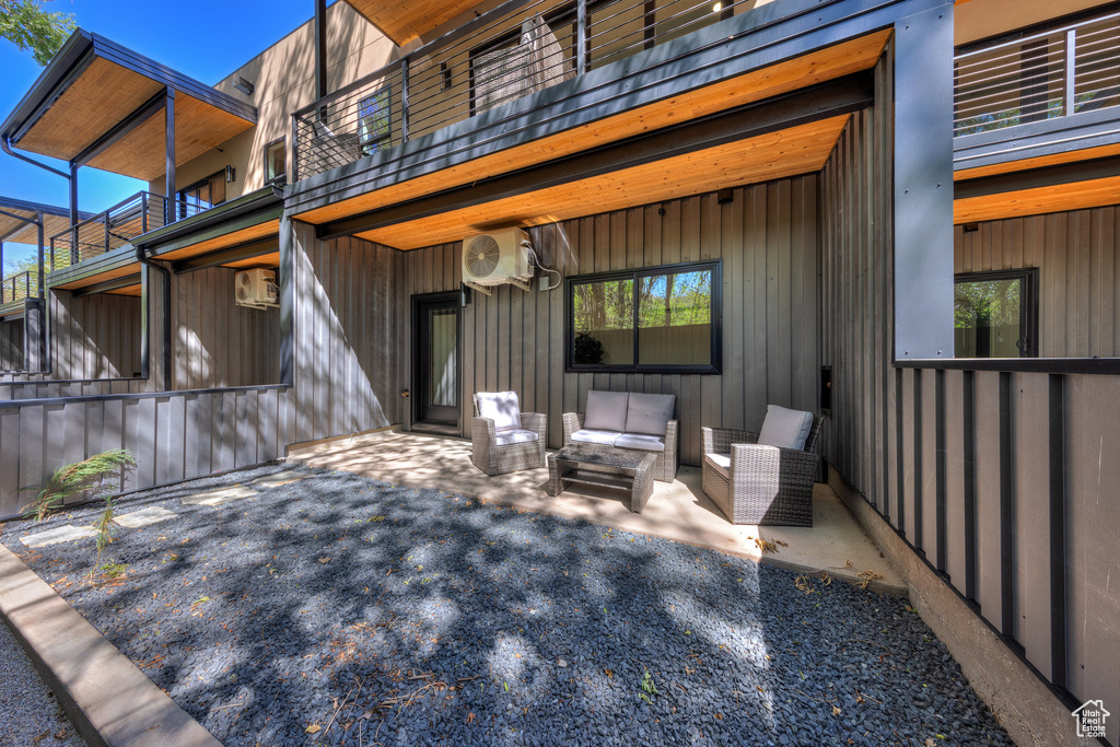 Exterior space featuring a balcony, an outdoor hangout area, an AC wall unit, and a patio area