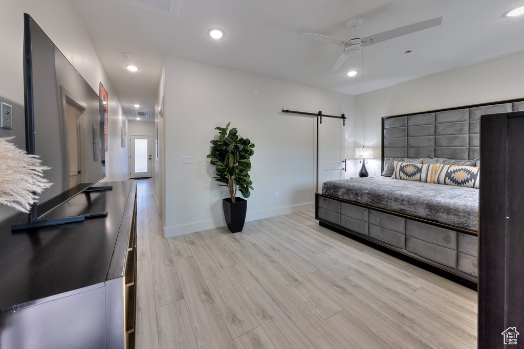Bedroom featuring a barn door, ceiling fan, and light wood-type flooring