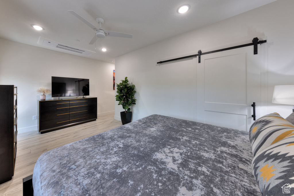 Bedroom featuring a barn door, ceiling fan, and light hardwood / wood-style flooring