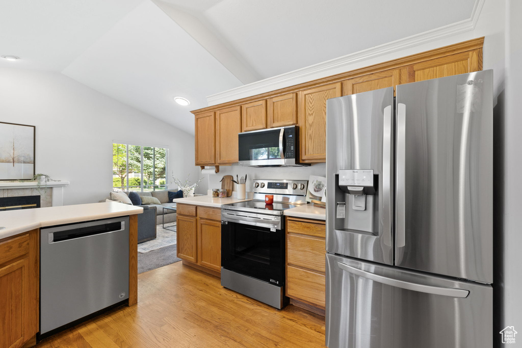 Kitchen with light hardwood / wood-style flooring, vaulted ceiling, and appliances with stainless steel finishes