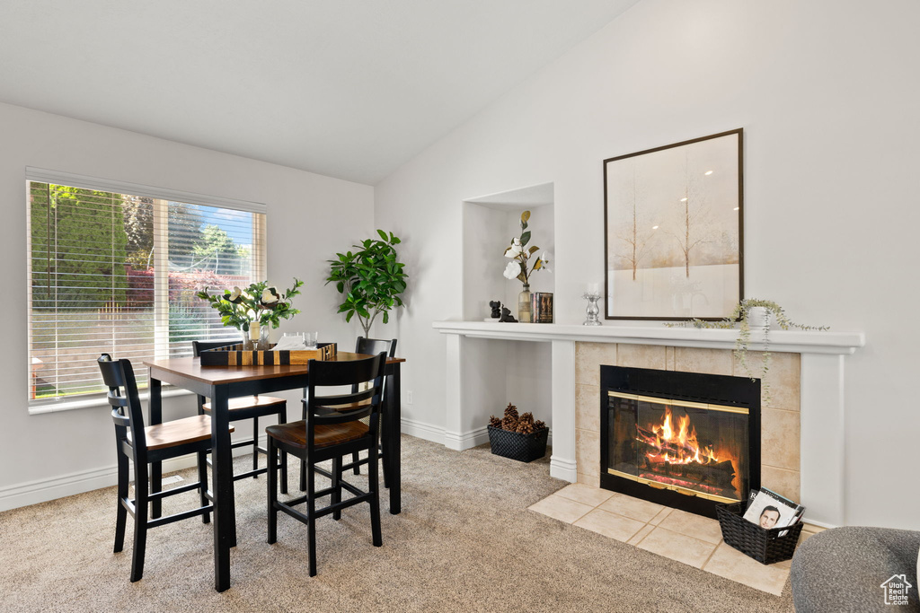 Dining area with lofted ceiling, light colored carpet, and a tiled fireplace